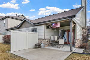 Back of house with a fire pit, fence, stone siding, roof with shingles, and a patio area