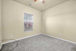 Carpeted spare room with visible vents, ceiling fan, and baseboards