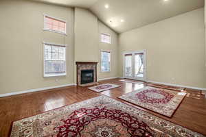 Living room featuring high vaulted ceiling, wood finished floors, a high end fireplace, and baseboards