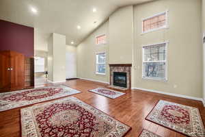 Living room featuring high vaulted ceiling, a notable chandelier, wood finished floors, baseboards, and a tiled fireplace