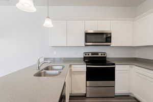 Kitchen featuring white cabinetry, stainless steel appliances, a sink, and decorative light fixtures