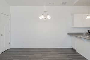 Unfurnished dining area featuring dark wood finished floors, visible vents, a sink, and baseboards