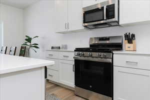 Kitchen featuring appliances with stainless steel finishes, wood-type flooring, white cabinetry, and backsplash