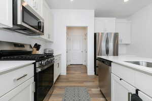 Kitchen featuring decorative backsplash, appliances with stainless steel finishes, white cabinets, and hardwood / wood-style floors