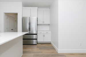 Kitchen with stainless steel refrigerator, hardwood / wood-style flooring, white cabinets, and decorative backsplash