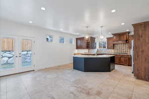 Kitchen with light stone counters, appliances with stainless steel finishes, decorative light fixtures, a kitchen island bar with sink, and backsplash