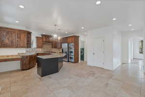 Kitchen featuring light stone counters, arched walkways, pendant lighting, open shelves, and an island bar with sink