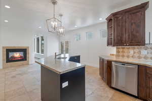 Kitchen with light stone counters, open shelves, decorative backsplash, stainless steel dishwasher, and an island bar with sink