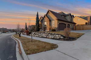 View of front of house with a garage, stone siding, concrete driveway, a residential view, and stucco siding