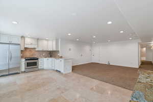 Kitchen featuring light colored carpet, appliances with stainless steel finishes, open floor plan, white cabinetry, and a sink