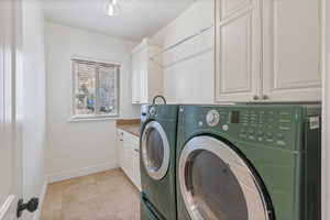 Clothes washing area with cabinet space, light tile patterned floors, baseboards, and washer and dryer