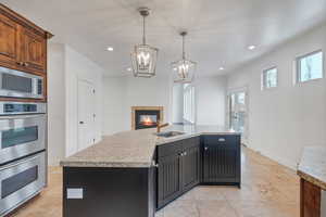 Kitchen with stainless steel appliances, a sink, an island bar with sink, a tiled fireplace, and decorative light fixtures