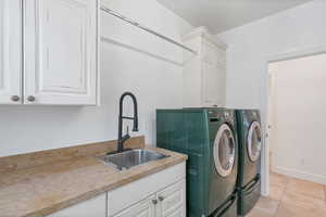 Laundry area featuring cabinet space, light tile patterned floors, separate washer and dryer, and a sink