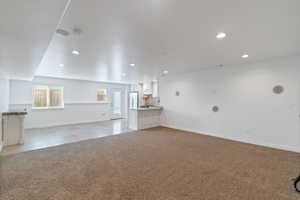 Unfurnished living room featuring recessed lighting, light colored carpet, baseboards, and light tile patterned floors, outside basement entrance.