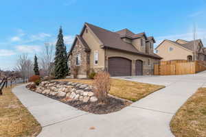 View of side of home with stone siding, driveway, an attached garage, and stucco siding