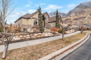 View of side of home featuring stucco siding, a lawn, fence, a mountain view, and stone siding