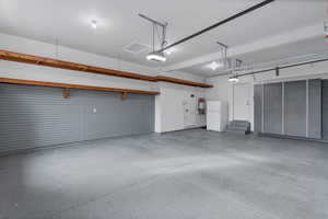 Custom 3 car Garage featuring garage door openers, custom cabinetry, epoxy flooring and freestanding refrigerator