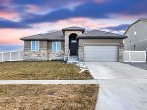 Prairie-style house featuring a garage, fence, driveway, stone siding, and stucco siding