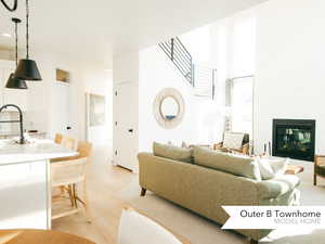 Living area with light wood-style flooring, stairs, and a glass covered fireplace