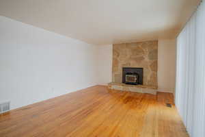 Unfurnished living room with a wood stove, light wood-style floors, and visible vents