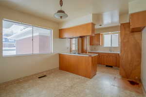 Kitchen with a peninsula, a sink, light countertops, brown cabinetry, and decorative light fixtures