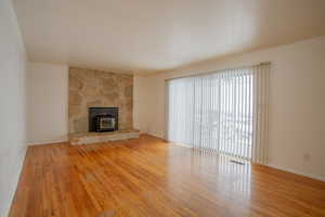 Unfurnished living room with visible vents, light wood finished floors, a wood stove, and baseboards