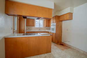 Kitchen with light countertops, brown cabinetry, a sink, white appliances, and a peninsula