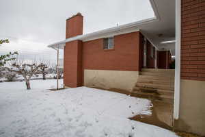 View of snowy exterior with a chimney and brick siding