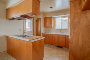 Kitchen featuring a peninsula, custom exhaust hood, light countertops, light floors, and a sink