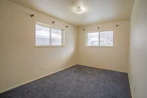 Spare room featuring baseboards, visible vents, dark colored carpet, and a wealth of natural light