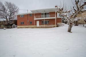 Snow covered property with a shed, brick siding, and a balcony