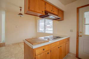 Kitchen with under cabinet range hood, white stovetop, light countertops, and brown cabinetry