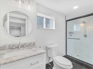 Bathroom featuring toilet, tile patterned floors, vanity, and a shower with shower door