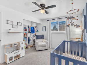 Carpeted bedroom with a crib, ceiling fan, and a closet