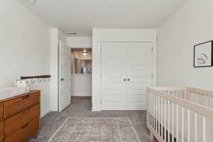 Carpeted bedroom with a closet, visible vents, a textured ceiling, a nursery area, and baseboards