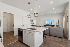 Kitchen featuring an island with sink, open floor plan, decorative light fixtures, a sink, and stainless steel dishwasher