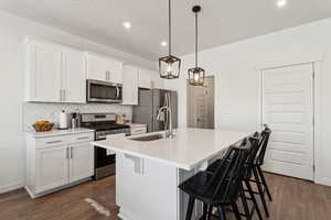 Kitchen with a breakfast bar area, stainless steel appliances, white cabinets, an island with sink, and decorative light fixtures