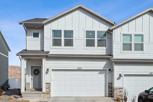 View of front of property featuring board and batten siding, stone siding, driveway, and a garage