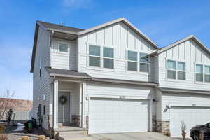 Townhome / multi-family property featuring board and batten siding, stone siding, driveway, and an attached garage