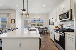 Kitchen with a breakfast bar area, decorative light fixtures, light countertops, appliances with stainless steel finishes, and a center island with sink