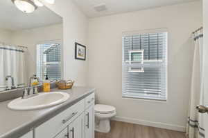 Bathroom featuring toilet, wood finished floors, visible vents, vanity, and baseboards