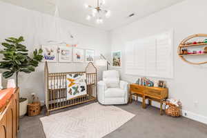 Carpeted bedroom with a nursery area, visible vents, baseboards, and an inviting chandelier