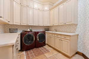 Laundry area featuring washer and clothes dryer, a sink, cabinet space, stone finish floor, and wallpapered walls