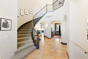 Entrance foyer featuring arched walkways, stone tile floors, stairway, a towering ceiling, and baseboards