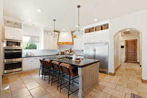 Kitchen with built in appliances, white cabinetry, custom exhaust hood, an island with sink, and dark countertops