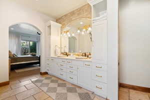 Full bath with a sink, ensuite bath, stone tile flooring, and baseboards