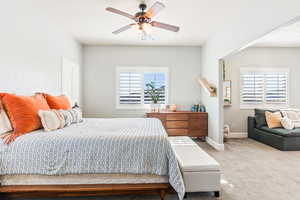 Bedroom featuring baseboards, multiple windows, a ceiling fan, and light colored carpet