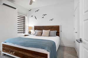 Carpeted bedroom with ceiling fan, baseboards, and an AC wall unit