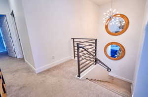 Hall with baseboards, an inviting chandelier, an upstairs landing, and light colored carpet