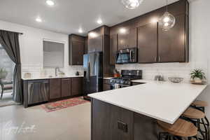 Kitchen with stainless steel appliances, a peninsula, a breakfast bar, hanging light fixtures, and light countertops